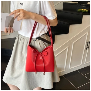 Détail d'un sac à bandoulière rouge avec décoration de nœud et écusson logo discret
