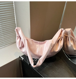 Detail of light pink glossy leather crescent bag with stitching on a dark surface