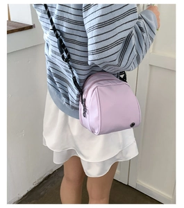 Detail view of a lavender shell-shaped nylon crossbody bag with sporty lettered straps