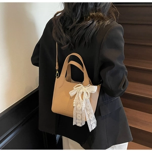 Detail of camel lychee leather bucket bag with lace bow and elegant pearl charm