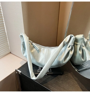 Detail of light blue pleated croissant bag showing glossy wax finish and knotted strap