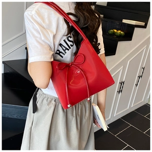 Détail du sac à bandoulière en cuir verni rouge avec nœud décoratif et pendentifs argentés