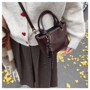 Détail du sac seau marron verni avec breloque raquette de tennis sur fond de feuilles d'automne