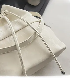 Close-up of cream drawstring bucket bag showing pleated texture and fine stitching