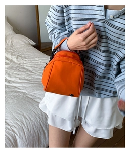 Detail of bright orange mini shell crossbody bag held by hand, showing nylon fabric texture