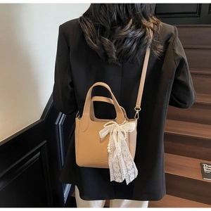 Close-up of litchi grain bucket bag with pearl lace bow detail worn with black suit