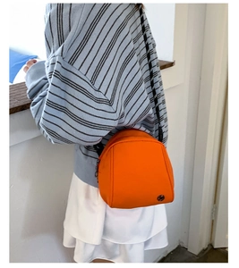 Close-up of bright orange shell bag crossbody with adjustable black strap and round logo