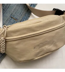 Close-up of beige nylon chest bag with embroidered logo and woven zipper pull detail