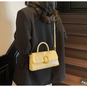 Détail du petit sac carré crème avec boucle dorée porté sur une veste de costume noire
