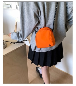 Detail view of the orange nylon shell bag showing the woven rope strap and logo patch