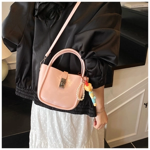 Detail view of pink bucket bag with pearl strap and cute doll pendant on a model