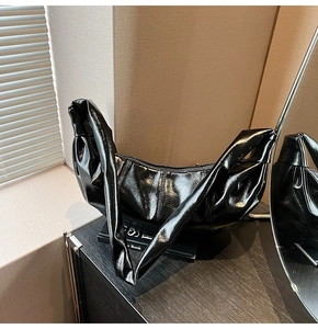 Detail of glossy black hobo bag featuring a unique knotted shoulder strap design