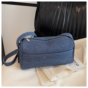 Detail of blue denim cylindrical shoulder bag showing washed texture and silver zipper