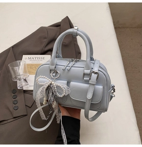 Detail of light blue Boston bag featuring front flap pockets and creative pearl lace charm