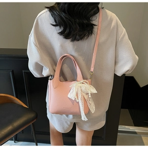 Detail of pink lychee leather handbag with decorative lace bow and pearl charm pendant