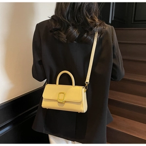 Vue mannequin d'un sac bandoulière crème avec boucle dorée sur un escalier en bois