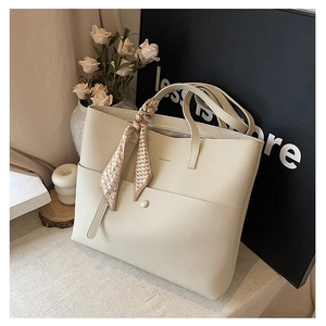 Close-up of cream tote bag featuring lychee grain leather, metal buckle and silk scarf detail