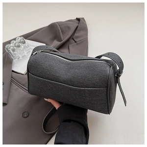 Detail of dark grey cylindrical denim crossbody bag featuring textured fabric and zipper