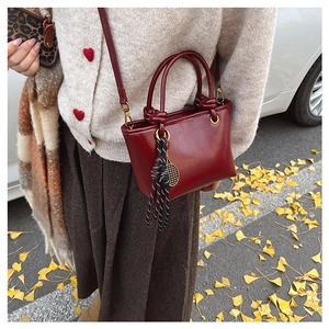 Gros plan sur un mini sac en cuir rouge foncé avec charme de raquette et pompon