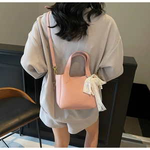 Detail of pink pebbled leather bucket bag with lace bow and pearl charm on a model
