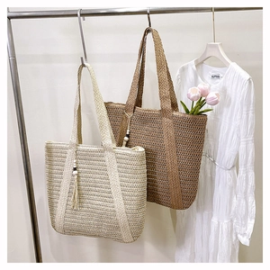 Detail of hand-woven straw tote bag with decorative tassel wood beads on metal rack