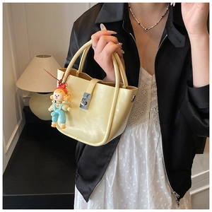 Close-up of a pale yellow leather bucket bag with silver turn-lock and cute charm