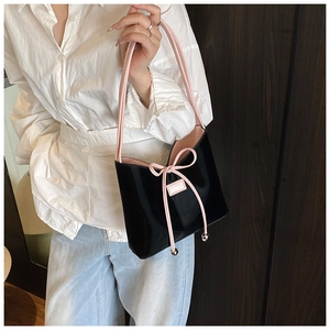 Détail du sac seau noir brillant avec un nœud rose et une doublure contrastée