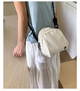 Detail of cream nylon shell bag with adjustable strap and decorative pompom charm