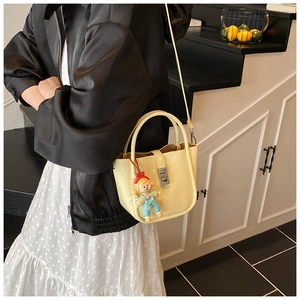 Detail of a creamy yellow matte leather bucket bag with silver buckle and cute doll charm