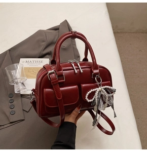Detail of dark red faux leather Boston bag with double pockets and pearl bow charm