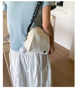 Detail of a beige shell-shaped crossbody bag with woven strap and white pompom charm