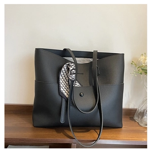 Close-up of black lychee leather tote bag with a decorative geometric silk scarf on handle