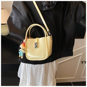 Close-up of pale yellow crossbody bucket bag with silver turn-lock and pearl doll charm
