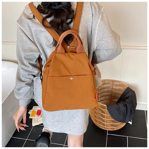 Detailed view of caramel nylon backpack with top handle and metal button front pocket