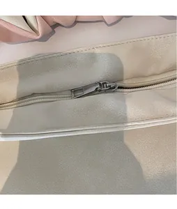 Macro shot of silver metal zipper pull and grainy leather texture on a white tote bag