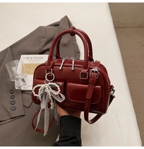 Detail of burgundy glossy leather Boston bag with a pearl bow charm and double metal zippers