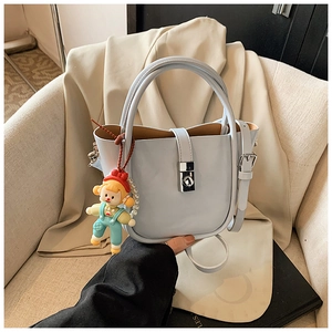 Detail of light blue bucket bag with silver metal lock and a cute cartoon doll pendant