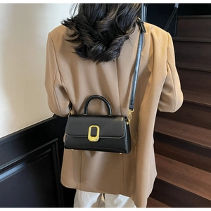 Détail du sac à bandoulière en cuir noir avec boucle dorée sur un mannequin
