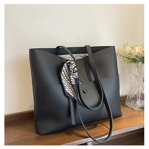 Close-up of black lychee grain tote bag with decorative silk scarf on a wooden shelf