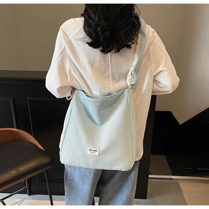 Light blue canvas hobo bag featuring wide shoulder strap and brand logo leather patch