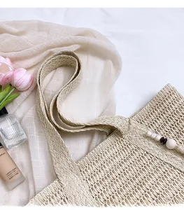 Detail of beige woven straw tote bag featuring decorative wooden bead tassels and handles