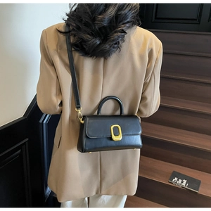 Détail d'un sac bandoulière noir minimaliste avec boucle dorée sur tenue élégante