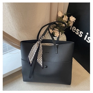 Detail of black pebbled leather tote bag with logo embossing and polka dot silk scarf