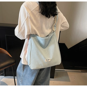 Detail of light blue hobo bag showing wide strap and woven MULAIDI logo tag