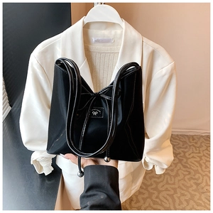 Détail du sac seau en cuir verni noir avec un nœud décoratif et de longues franges à glands