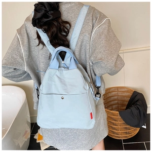 Rear view of a light blue nylon crossbody chest bag worn by a model in a cozy indoor setting