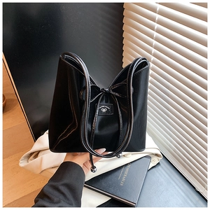 Détail du sac seau noir brillant avec un nœud décoratif et une finition de qualité