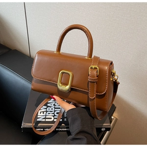 Gros plan du sac en cuir marron avec boucle en métal doré sur un livre moderne