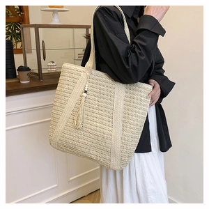 Detail of a beige woven straw tote bag with decorative tassels and wooden beads