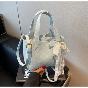 Detail of light blue bucket bag with pebble leather, pearl bow charm, and gold hardware